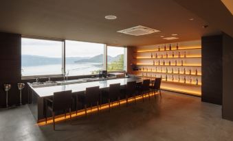 a modern bar with a long counter , several chairs , and a view of the ocean at WE Hotel Toya