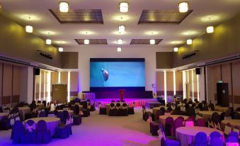 a large event space with multiple tables and chairs set up for a gathering , including a stage with a screen and a projector at Hotel Grand Baron