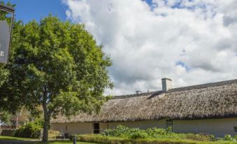 a thatched - roof building with a tree in front and clouds in the sky above at The Anchorage Hotel