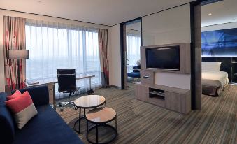 a hotel room with a large window , a flat - screen tv mounted on the wall , and a desk with a computer at Novotel Taipei Taoyuan International Airport