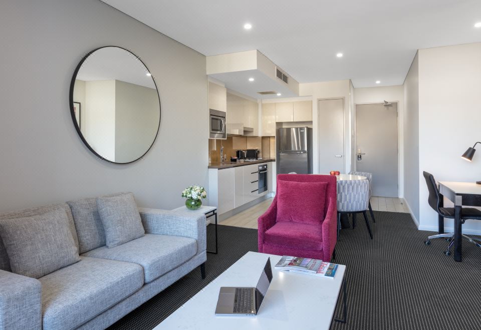 a modern living room with a pink chair , white couch , and a circular mirror on the wall at Meriton Suites North Ryde