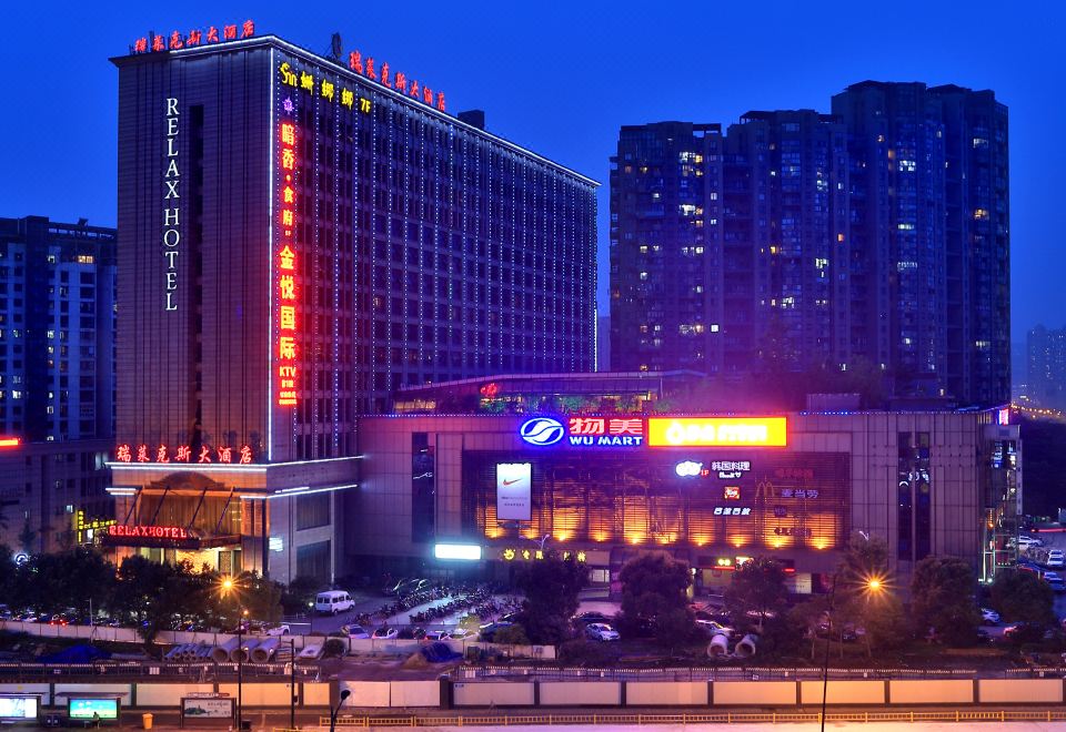 a large building with a red sign is lit up at night in front of other buildings at Relax Hotel