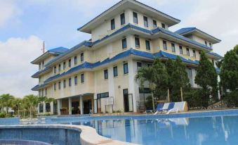 a large , white building with blue accents is surrounded by a swimming pool and lounge chairs at Grand Elty Singgasana Hotel