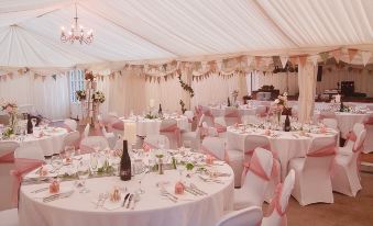 a large dining room with multiple round tables covered in white tablecloths and adorned with pink and white decorations at St Quintin Arms