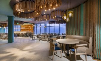 a modern restaurant with wooden chairs and tables , pendant lights , and a large window overlooking the city at Dongji Island Dongguan Hotel