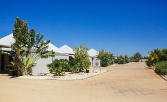 a white tent is set up on a sandy area next to some trees and shrubs at Exmouth Escape Resort