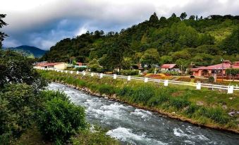 a river flows through a rural area with houses and trees on a hillside in the background at Hotel Ladera