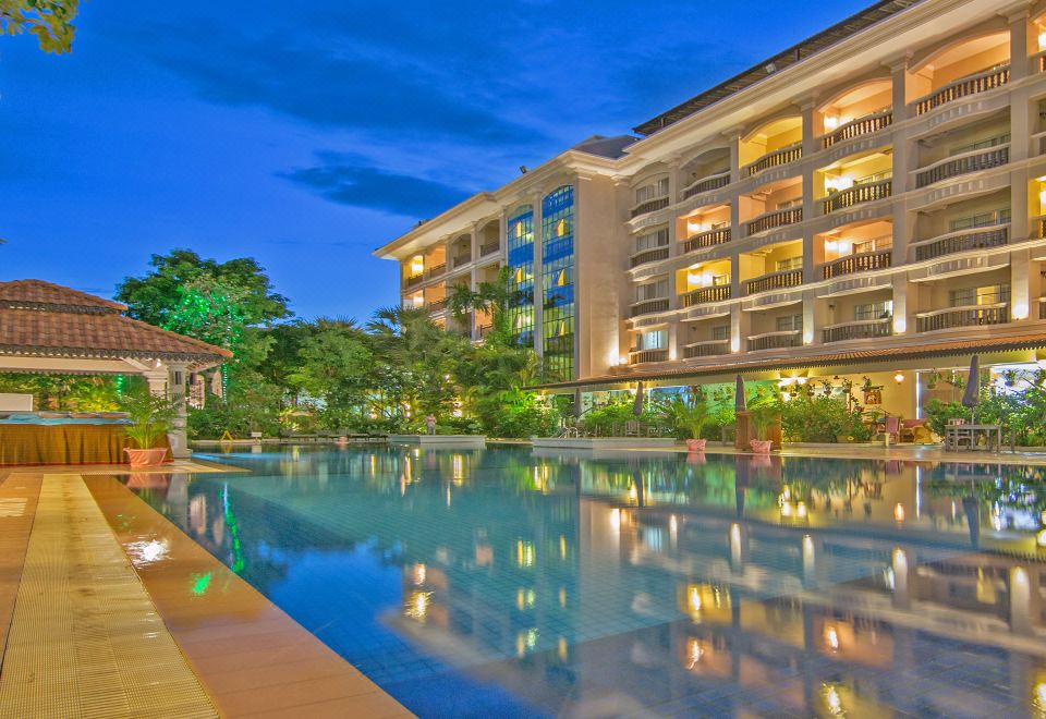 a large hotel building with a swimming pool in front of it , surrounded by trees and grass at Hotel Somadevi Angkor Resort & Spa