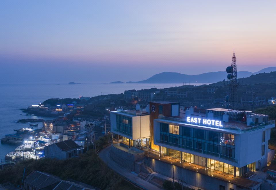 a modern hotel building with a blue sign , surrounded by mountains and the sea at dusk at Dongji Island Dongguan Hotel
