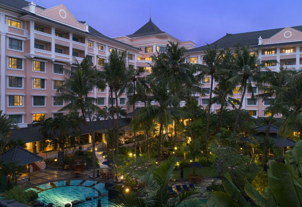 a large hotel with a pool and palm trees is lit up at night , surrounded by palm trees at Melia Purosani Yogyakarta