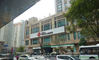 There is a large building with parked cars and pedestrians walking on the street outside at Home Inn Selected (South Square of Shanghai Railway Station)