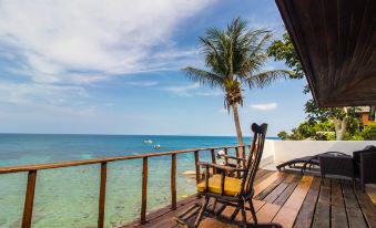 a wooden deck overlooking the ocean , with a rocking chair and a surfboard placed on it at Taatoh Seaview Resort