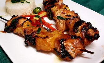 a white plate with two skewers of meat , rice , and vegetables on it , placed on a dining table at The Lamb Inn