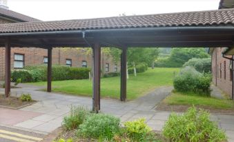 a covered walkway surrounded by green grass and trees , with a brick building in the background at Premier Inn Dover East