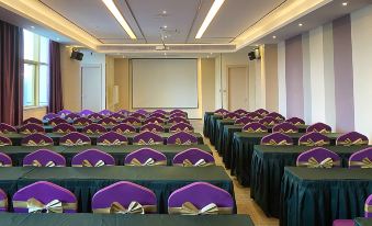 Rows of purple chairs face the front of a large event, where green tablecloths are used at Lavande Hotel