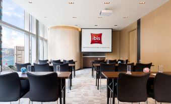 There is a restaurant with tables and chairs in front, facing a large screen on the wall behind it at ibis Hong Kong Central and Sheung Wan Hotel