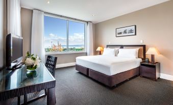 a large bed with white sheets is in a room with a desk and chair , next to a window at Hilton Lake Taupo