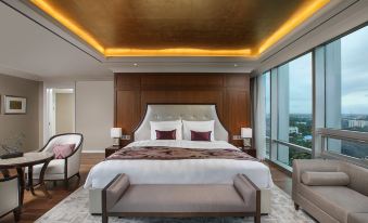 a luxurious bedroom with a large bed , two chairs , and a view of the city outside the window at Lotte Hotel Yangon