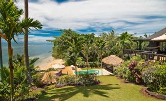 a luxurious villa with a pool and lush tropical vegetation overlooks the ocean , where a swimming pool is surrounded by lounge chairs at Taveuni Palms Resort