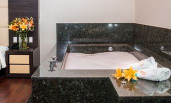 a bathtub filled with water and surrounded by a black granite countertop , with a flower arrangement on the side at Hotel Astor