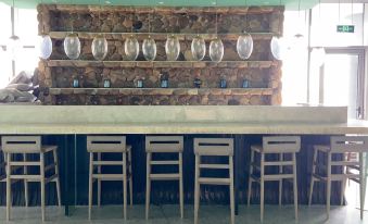 a bar with wooden chairs and a stone wall , featuring several hanging lights and wine glasses at Dongji Island Dongguan Hotel