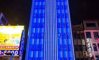 a tall building with a blue light display on its side , surrounded by other buildings and advertisements at Airline Inn Kaohsiung Station