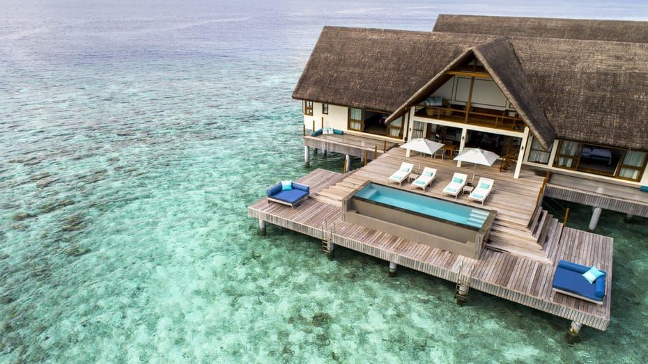 a wooden deck with a hot tub and lounge chairs overlooks a blue ocean , where a house is situated at Four Seasons Resort Maldives at Landaa Giraavaru