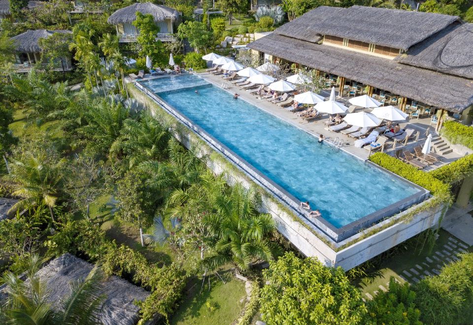a large swimming pool with a long , rectangular shape is surrounded by trees and lounge chairs at Lahana Resort Phu Quoc & Spa