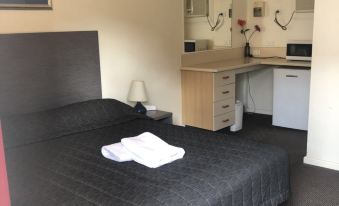 a neatly made bed with a black headboard and white towels on top , next to a desk with a microwave and cabinet at Westside Motor Inn