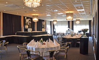 a large , well - lit banquet hall with multiple dining tables and chairs , all set for a formal event at Fletcher Hotel - Restaurant Heiloo