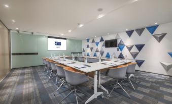 The conference room is equipped with blue chairs, a long table, and a large presentation screen on the front wall at Holiday Inn Express Shanghai Gubei