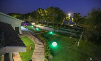 a well - lit garden area with green grass , trees , and lights at night , as well as a path leading to a building at Lucen