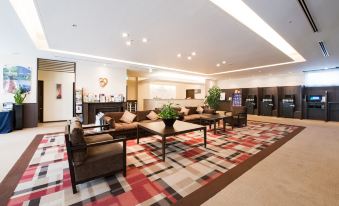a spacious and well - lit hotel lobby with multiple couches , chairs , and tables , as well as a television at Daiwa Roynet Hotel Oita