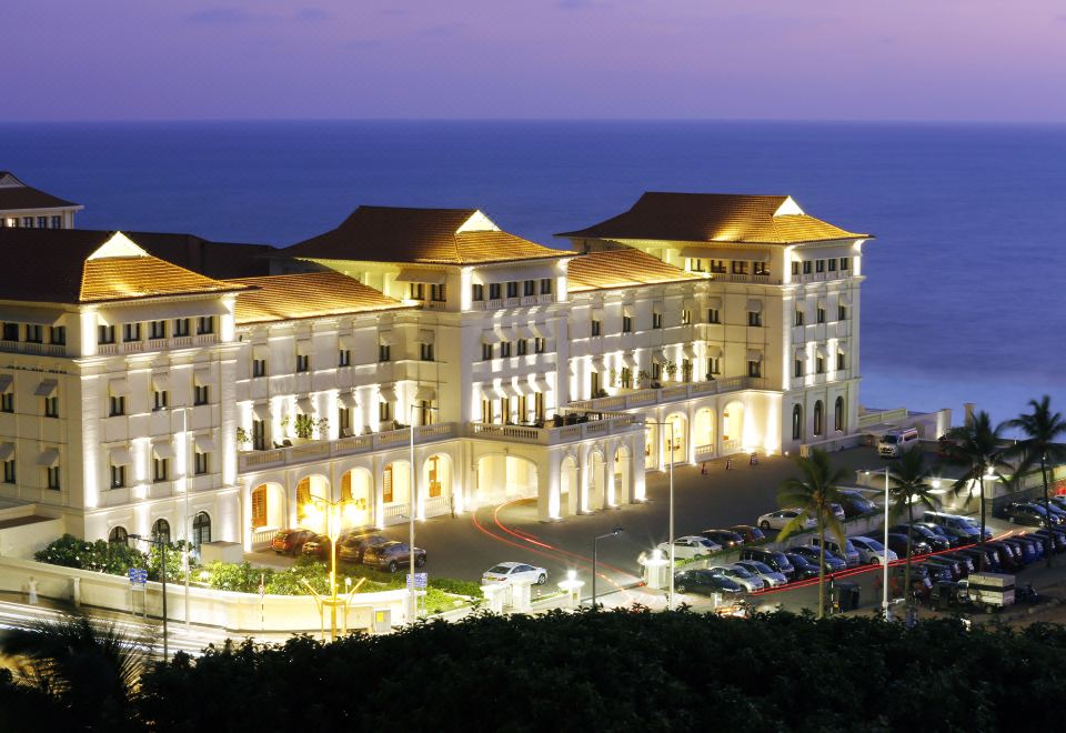 a large , ornate hotel building with multiple floors and balconies , situated near the ocean at night at Galle Face Hotel