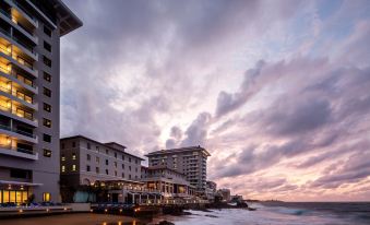 a large building is situated on the beach , with a sunset in the background and clouds at Condado Vanderbilt Hotel