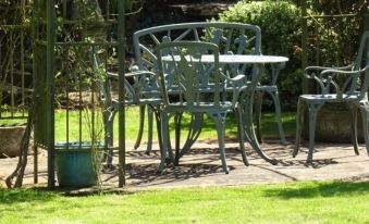 a green metal table and chairs set in a garden , surrounded by grass and trees at Moor Court Farm