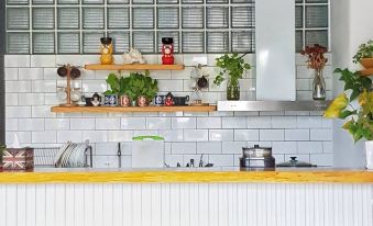 a white kitchen counter with wooden stools and a hanging light fixture , featuring various potted plants and dishes on the shelves at Red House