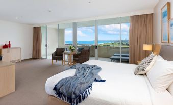 a bedroom with a bed , two chairs , and a view of the ocean through large windows at Sage Hotel Wollongong