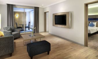 a modern living room with a large flat - screen tv mounted on the wall , a wooden floor , and a couch at Novotel Jakarta Mangga Dua Square