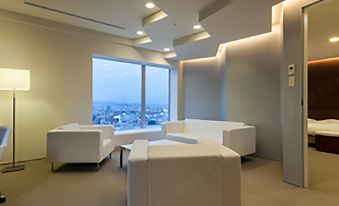 a modern living room with white sofas , a coffee table , and large windows overlooking the city at Daiwa Roynet Hotel Numazu