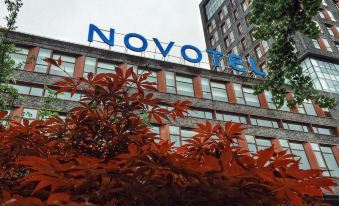 The front view of the hotel features a sign in the foreground and illuminated trees on both sides at Novotel Shanghai Clover
