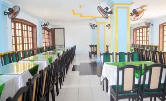 a long dining table with chairs and green tablecloths in a restaurant setting , surrounded by white walls at Cay Thong Hotel