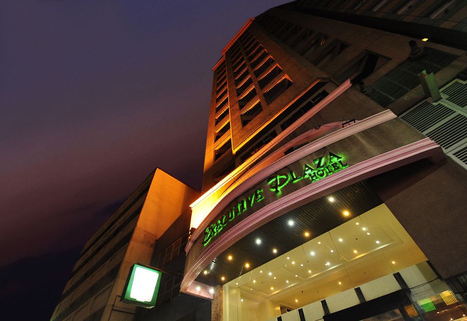 "a tall building with a green sign that reads "" executive plaza "" prominently displayed on the front of the building" at Executive Hotel