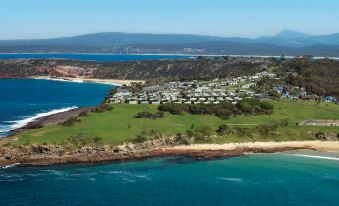 an aerial view of a coastal town with a beach , green grass , and buildings near the water at NRMA Merimbula Beach Holiday Resort