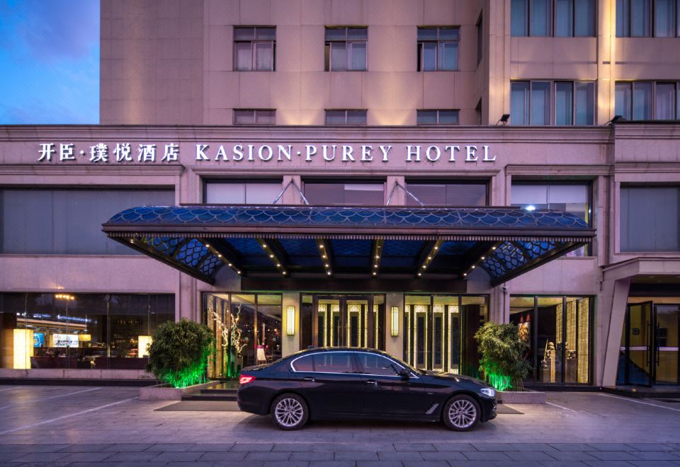 There is a hotel entrance with an illuminated sign above it, and there is another building in front of it at Kasion Purey Hotel (Yiwu International Trade City store)