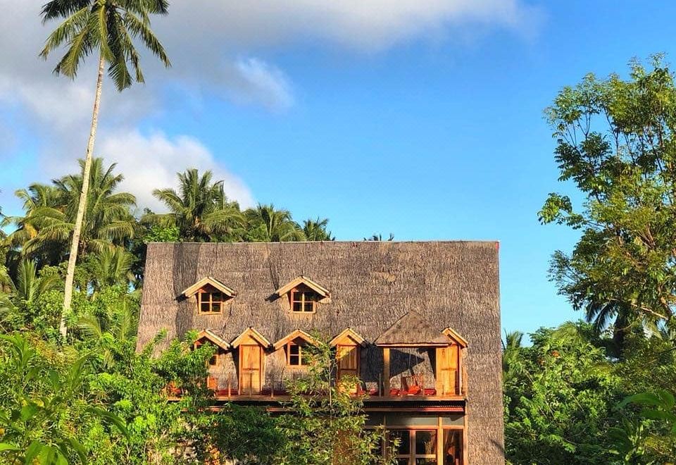 a tropical resort with a wooden building surrounded by lush greenery and palm trees under a blue sky at Volcano House