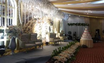 a large event space decorated with white chairs , flowers , and chandeliers , giving it an elegant and romantic atmosphere at Grand Elty Singgasana Hotel