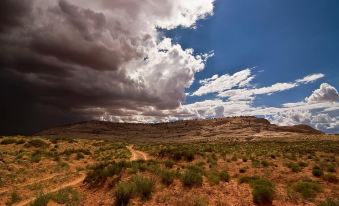 a desert landscape with a dirt road winding through it , leading to a large stormy sky at Moenkopi Legacy Inn & Suites