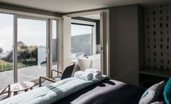 a modern bedroom with large windows offering views of the outdoors , featuring a comfortable bed and a chair at Lakestone Lodge