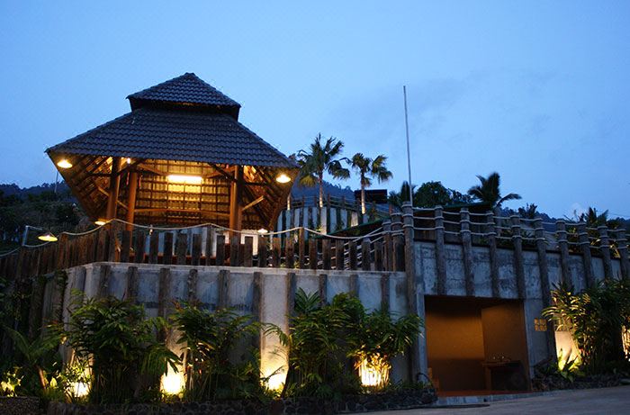 a wooden building with a thatched roof , surrounded by palm trees and lit up at night at The Waterway Villa